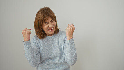 A joyful mature woman celebrates with clenched fists against a white background exuding happiness...