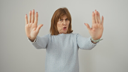 Middle-aged woman making stop gesture with both hands against isolated white background, expressing refusal or boundaries.