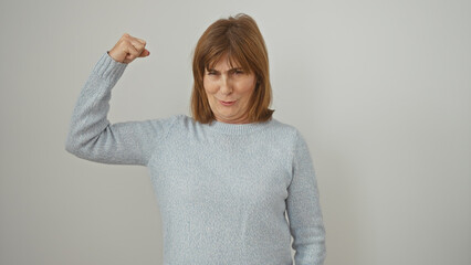 Confident middle-aged woman flexing her arm muscle against a white background, showcasing strength...