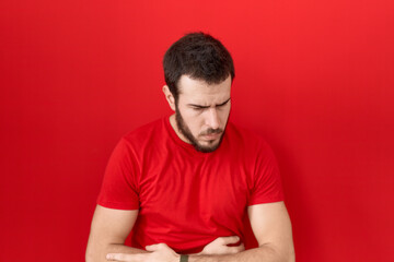 Obraz premium Young hispanic man wearing casual red t shirt with hand on stomach because indigestion, painful illness feeling unwell. ache concept.
