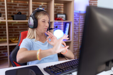 Young caucasian woman playing video games wearing headphones disgusted expression, displeased and...