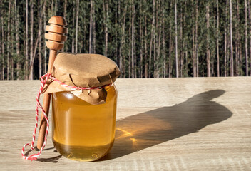 pot of honey on a wooden table and a eucalyptus forest in the background, in Brazil