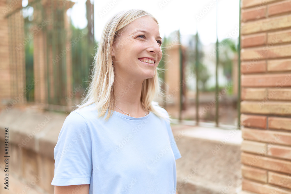 Wall mural Young blonde woman smiling confident looking to the side at street