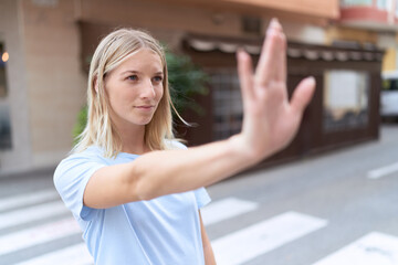 Young blonde woman doing stop gesture with hand at coffee shop terrace