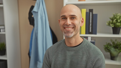 Handsome bald man with beard smiling indoors wearing casual sweater in a tidy living room
