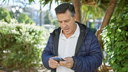 Mature man texting on smartphone in a sunlit park