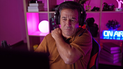 Mature man with headphones in a modern gaming room looking tired during a night session