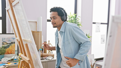 Handsome man with headphones painting on an easel in a bright studio
