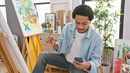 A thoughtful young man checking his smartphone in a bright art studio.