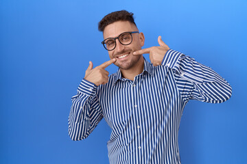Hispanic man with beard wearing glasses smiling cheerful showing and pointing with fingers teeth and mouth. dental health concept.