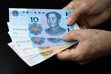 Elderly woman with yuan banknotes in wrinkled hands. Concept of pension payments in China, savings...