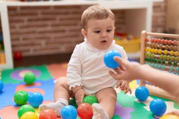 Fototapeta premium Adorable toddler playing with balls sitting on floor at kindergarten