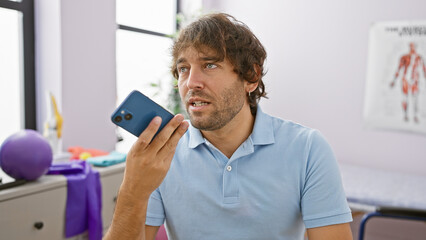 Handsome bearded man using smartphone in rehabilitation clinic interior, portraying healthcare...