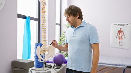 Attractive bearded man examines a spinal model in a brightly lit rehabilitation clinic