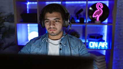 Focused man wearing headphones streams in a neon-lit gaming room at night.