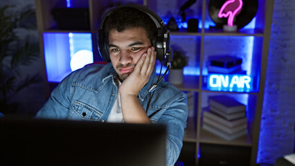 A bored young man wearing headphones in a neon-lit gaming room at night with technology ambiance