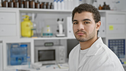 Arab man in white lab coat posing confidently in a chemistry laboratory setting stocked with...