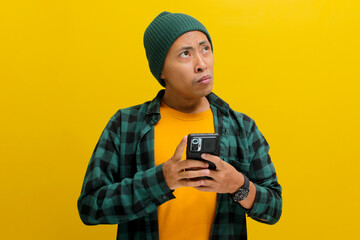 An uninterested and bored Asian man, dressed in a beanie hat and casual shirt, uses his mobile...