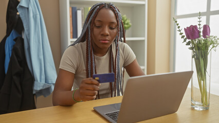 African american woman with braids shopping online with a credit card in a modern home interior.
