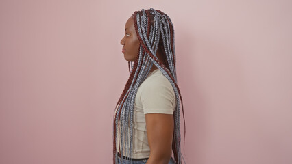 Serene african american woman with stylish braids posing against a pastel pink isolated background, embodying elegance.