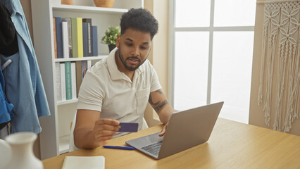 African american man using credit card for online shopping at home on laptop in a well-organized...