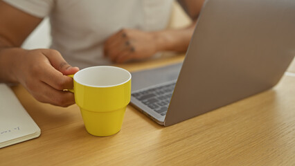 Close-up of african american man using a laptop at home with a coffee cup