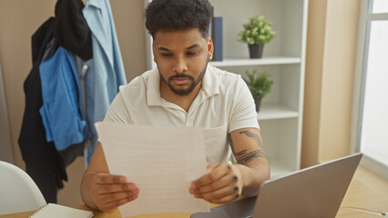 Handsome man reading document in a modern living room with laptop and greenery
