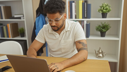 Focused man with glasses working on laptop in a modern home office.