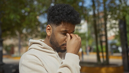 Stressed african american man pinching bridge of nose in outdoor city park setting.