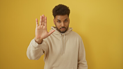 African american man in hoodie gesturing stop against yellow background