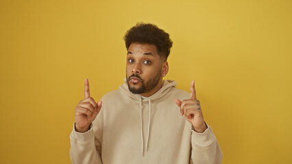 Handsome adult black man pointing upwards isolated against a vibrant yellow background