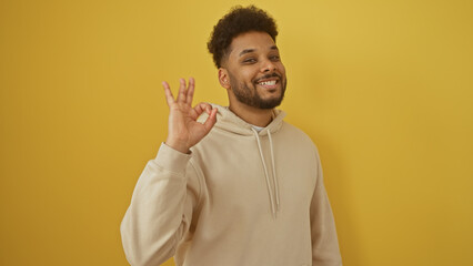 Smiling african american man giving okay gesture isolated on a yellow background