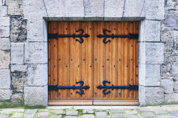 A rustic medieval wooden door with black iron hinges set in an ancient stone wall.