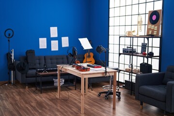 A stylish music studio setup with a blue wall, featuring a guitar, microphone, headphones, and sheet music on a wooden table.