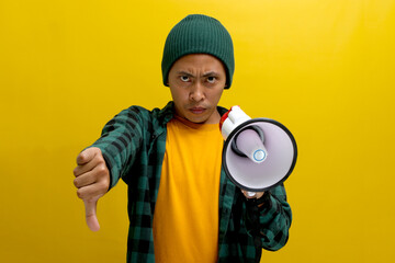 Displeased Asian man in a beanie hat holds a megaphone with an angry face, showing a thumbs-down to...