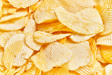 Close-up of crispy potato chips piled together, capturing details of their ridged texture and...