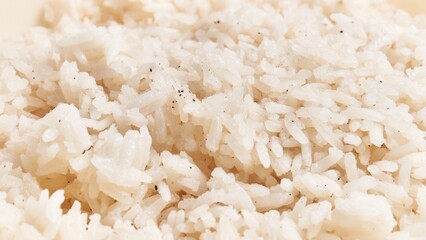 Close-up of cooked white basmati rice grains with visible seasoning specks on a plain background.