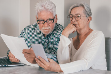 Elderly senior family couple reading paper correspondence or mails, sitting at home with computer....