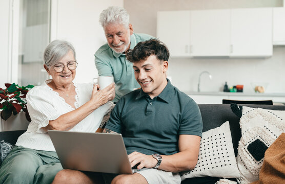 Happy multigenerational family, grandparents learning new computer technology from experienced young grandson teaching how to use computer, how to make online shopping, book travel and vacation