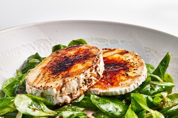Grilled goat cheese on a bed of fresh spinach leaves, garnished with balsamic reduction.