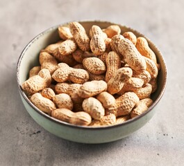 A bowl filled with whole peanuts on a textured grey surface, suggesting healthy, raw food.