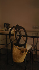 Straw bag hanging on a black wooden chair in a minimalist interior setup with metal table.