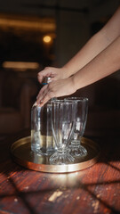 A woman sets empty glasses on a tray, preparing for a beverage service indoors.