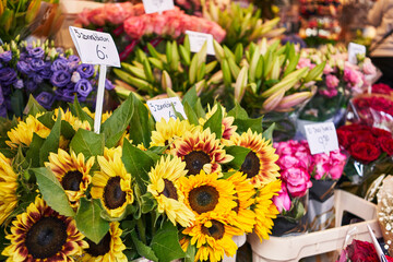 Colorful sunflowers and assorted bouquets with price tags at a vibrant outdoor flower market.