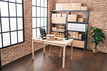 A modern office with computer, packages, shelves, plant, desk, barcode, brick wall, window, and...