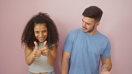 A cheerful woman and a man gesture thumbs up together against a pink isolated background,...