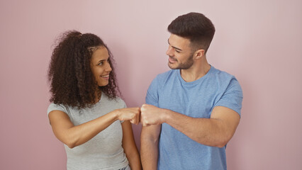 A joyful woman and man fist-bumping against a plain pink background, depicting a positive relationship.
