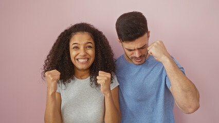 A joyful woman and man celebrate with raised fists against a pink isolated background, portraying...