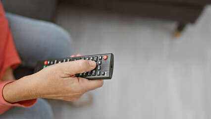 Middle-aged woman holding a remote control in a modern living room setting, exemplifying leisure or...