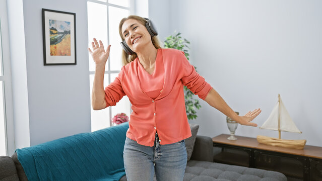 Smiling woman with headphones enjoying music and dancing in a bright living room